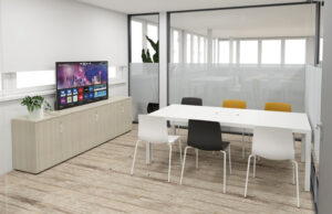 Sala de reuniones con televisor sobre aparador de madera clara y mesa blanca con sillas