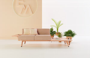 Sofá modular rosa con bandejas laterales y jardineras ante un panel con logotipo