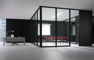 Sala de reuniones acristalada con perfilería negra, sillas rojas y pantalla de proyección