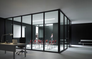 Sala de reuniones acristalada con perfilería negra y sillas rojas, con dos personas dentro