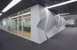 Sala de reuniones acristalada junto a un volumen blanco con relieve geométrico