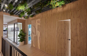 Pasillo con revestimiento acústico de lamas de madera, panel decorativo recortado y vegetación en el techo