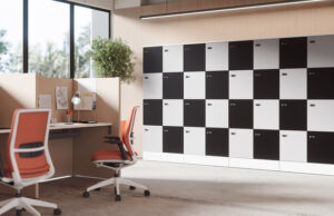 Pared de taquillas en damero blanco y negro junto a puestos con mamparas y sillas naranjas