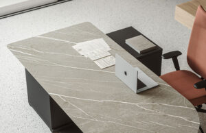 Detalle de mesa de dirección con tablero de piedra veteada, portátil y silla terracota