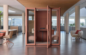Cabina de reuniones color terracota con la puerta abierta, butacas y mesa, en un vestíbulo