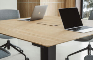 Detalle de mesa de reuniones de madera con dos portátiles y tapa de conexiones