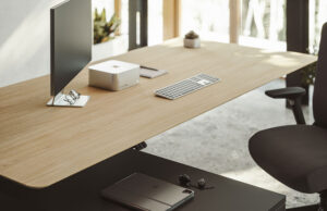 Detalle de mesa elevable de madera con monitor, teclado y silla oscura