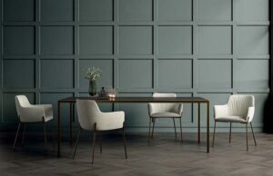 Mesa de comedor con sillas tapizadas claras ante una pared verde con molduras