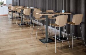 Cafetería con mesas altas y taburetes de madera junto a una pared de lamas