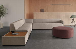 Sofá modular en L beis con puf redondo granate ante una pared de madera