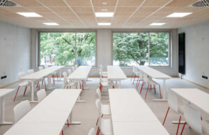 Aula luminosa con mesas blancas, sillas de patas rojas y techo acústico