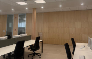 Sala de trabajo con revestimiento mural de madera de suelo a techo y puestos con sillas negras
