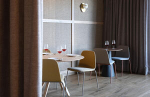 Comedor con mesas redondas, sillas tapizadas en mostaza, verde y azul y cortinas