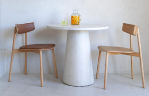 Dos sillas de madera, una tapizada en cuero marrón y otra de asiento de madera, junto a una mesa redonda blanca