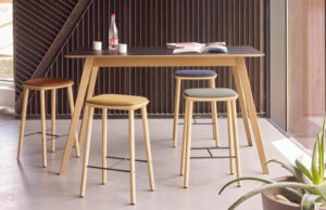 Mesa alta de tablero negro con patas de madera y taburetes de asientos de colores