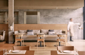 Restaurante con banco corrido tapizado, mesas redondas, sillas de madera y muro de hormigón