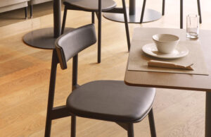 Detalle de silla oscura tapizada junto a una mesa de restaurante con vajilla